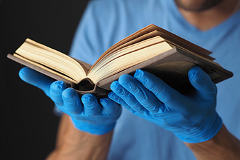 Book in men's hands in blue medical gloves.