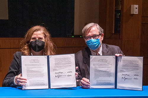 Two people sitting at table holding signed documents.