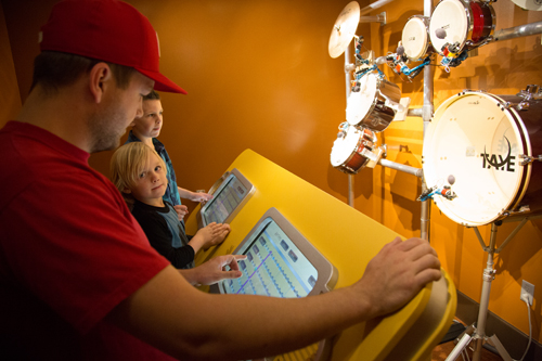 A man and two kids use touchscreen interface connected to drums.