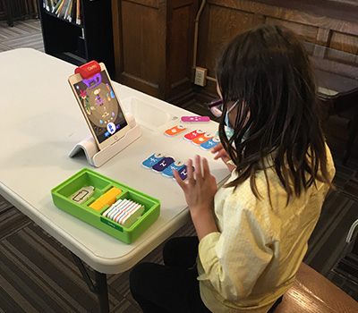 girl sitting at table and playing game on tablet