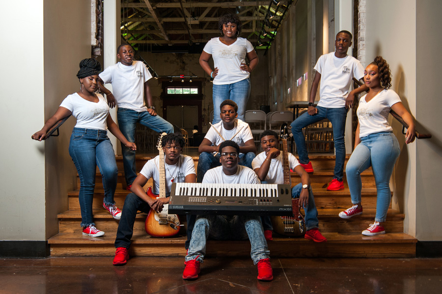 A group of gifted and talented teenagers, dressed in blue jeans and white shirts, pose with musical instruments on stage at the The B.B. King Museum and Delta Interpretive Center.