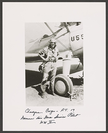 Charlyne Creger wearing a flight suit and goggles and carrying a rucksack posing in front of an airplane