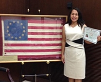Susan Simons holds her U.S. Naturalization certificate in front of a historical American flag