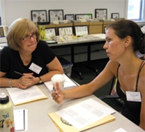 Two teachers converse at a table; musuem collections are visible in the background.