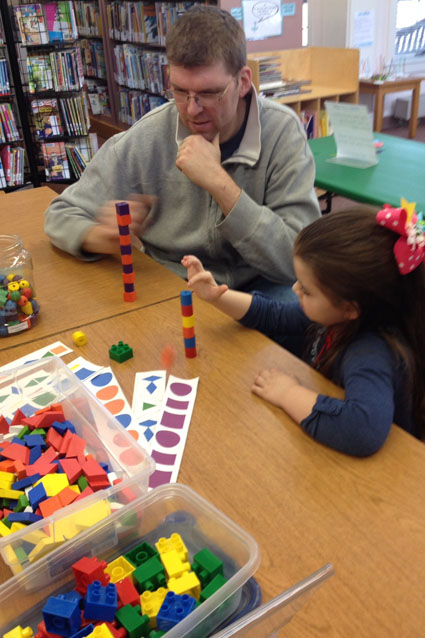 A young learner and her guardian learn about patterns and build towers at a Kingdom of Why science station.