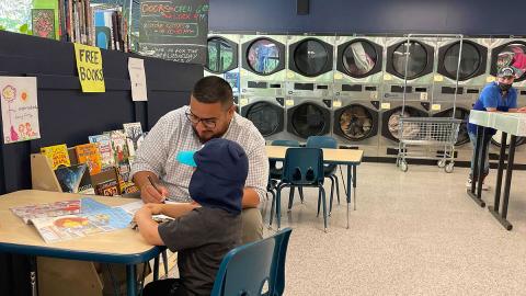 Wash and Learn library participants engage in table activity and a row of coin laundry machines in the background.