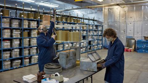 Film archivists recanning and cleaning Pakistani films. Shelving units in background hold processed Indian films. Photo courtesy of The George Eastman Museum