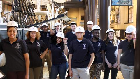 Group of students wearing hard hats, standing in front of museum exhibit.