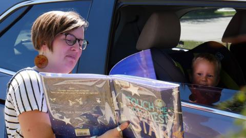 Staff reading book to toddler in a car seat for the Kenosha Public Library Drive Thru Storytime