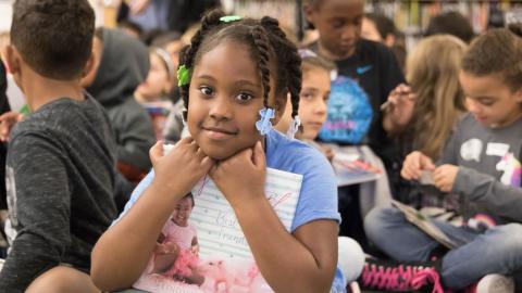 A young reader poses with a book she plans to check out during one of Sacramento Public Library’s Book First programs